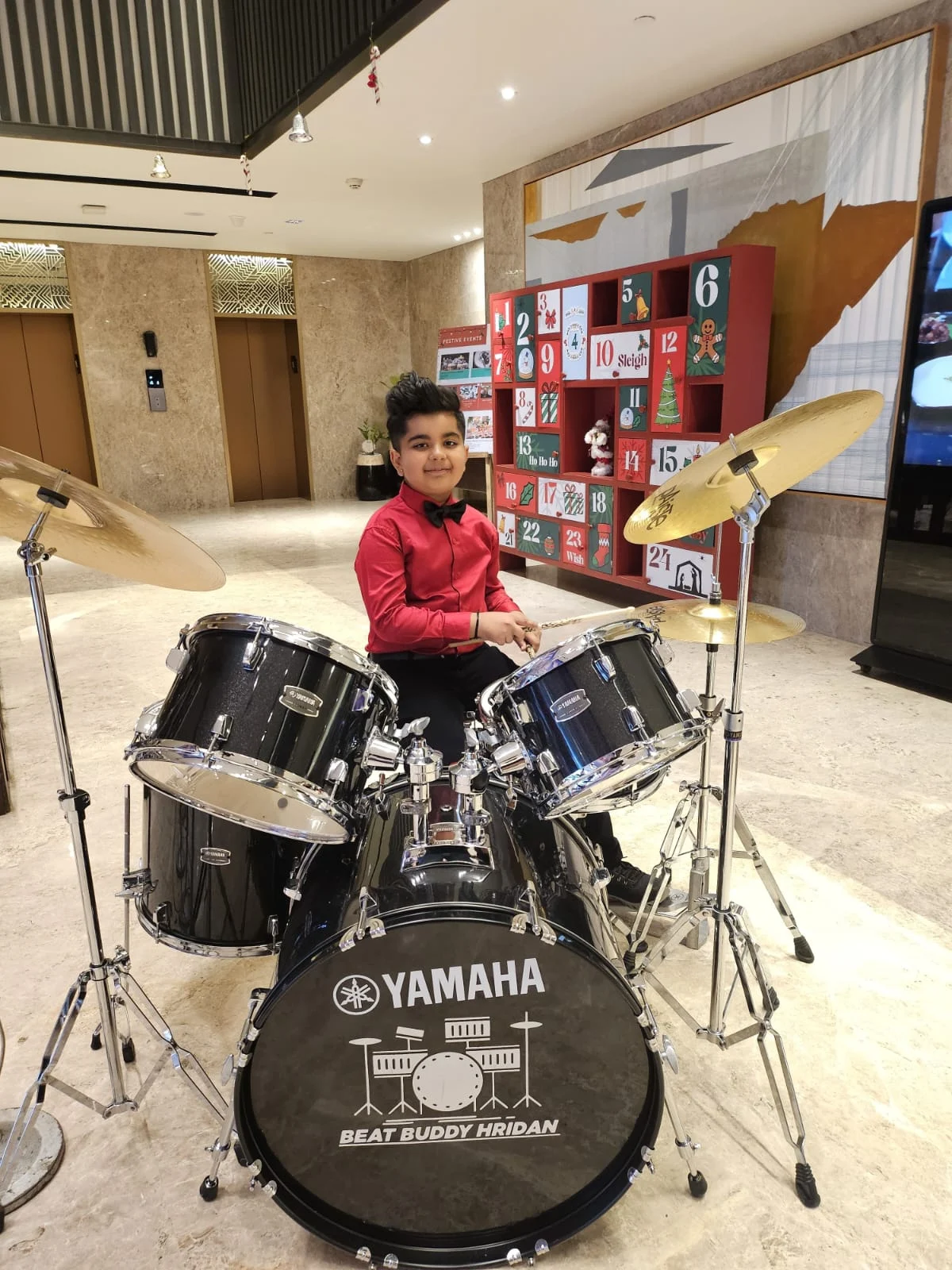 Hridan wearing a red shirt and sitting at a Yamaha drum kit